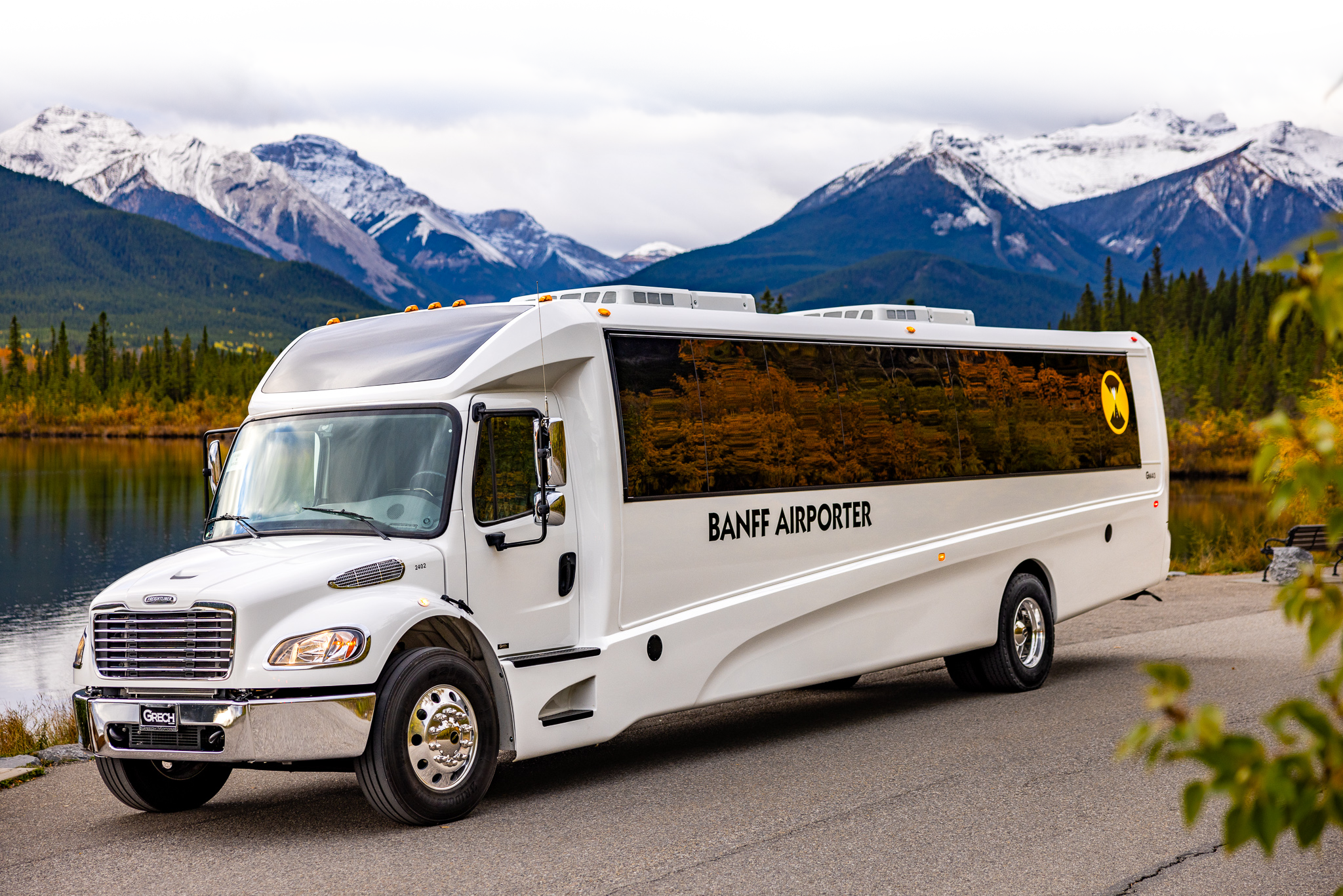 Banff Airporter shuttle bus parked by a lake with snow-capped Rocky Mountains behind it